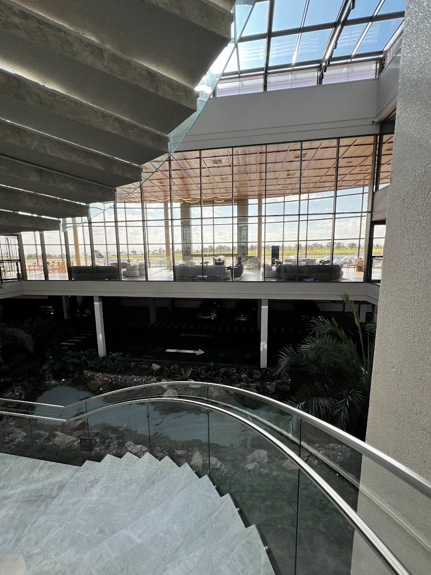 Escada de mármore com guarda-corpo de vidro e jardim interno de pedras, vista do mezanino