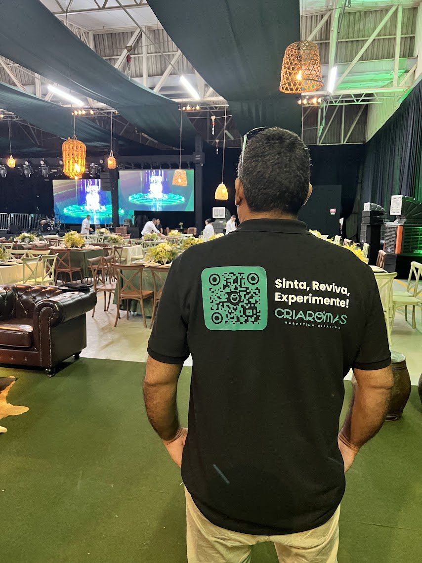 Pessoa de costas em evento da marca, com camiseta da CriAromas escrita Sinta, Reviva, Experimente