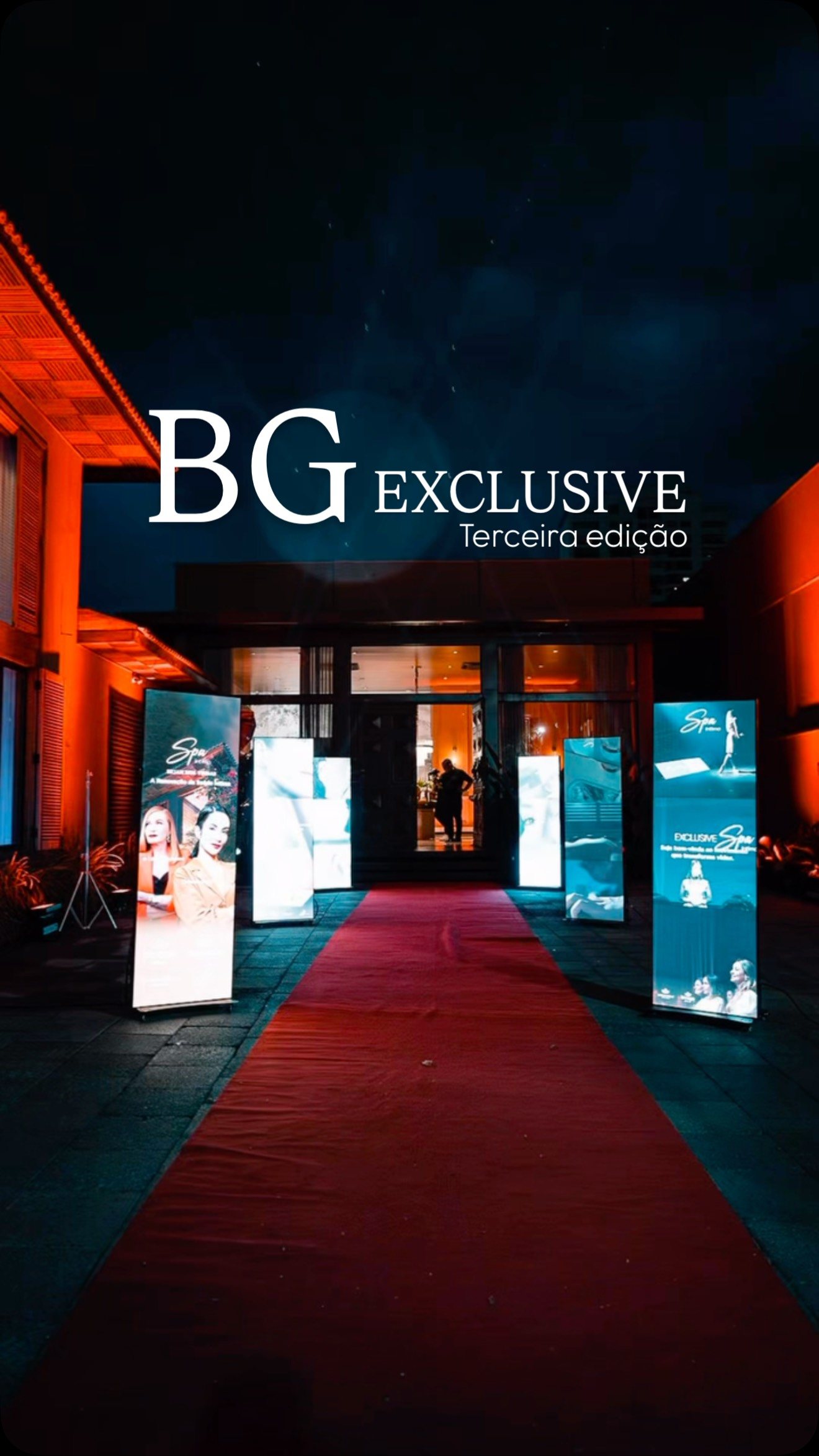 Entrada do evento à noite, tapete vermelho e totens iluminados sob o letreiro BG Exclusive